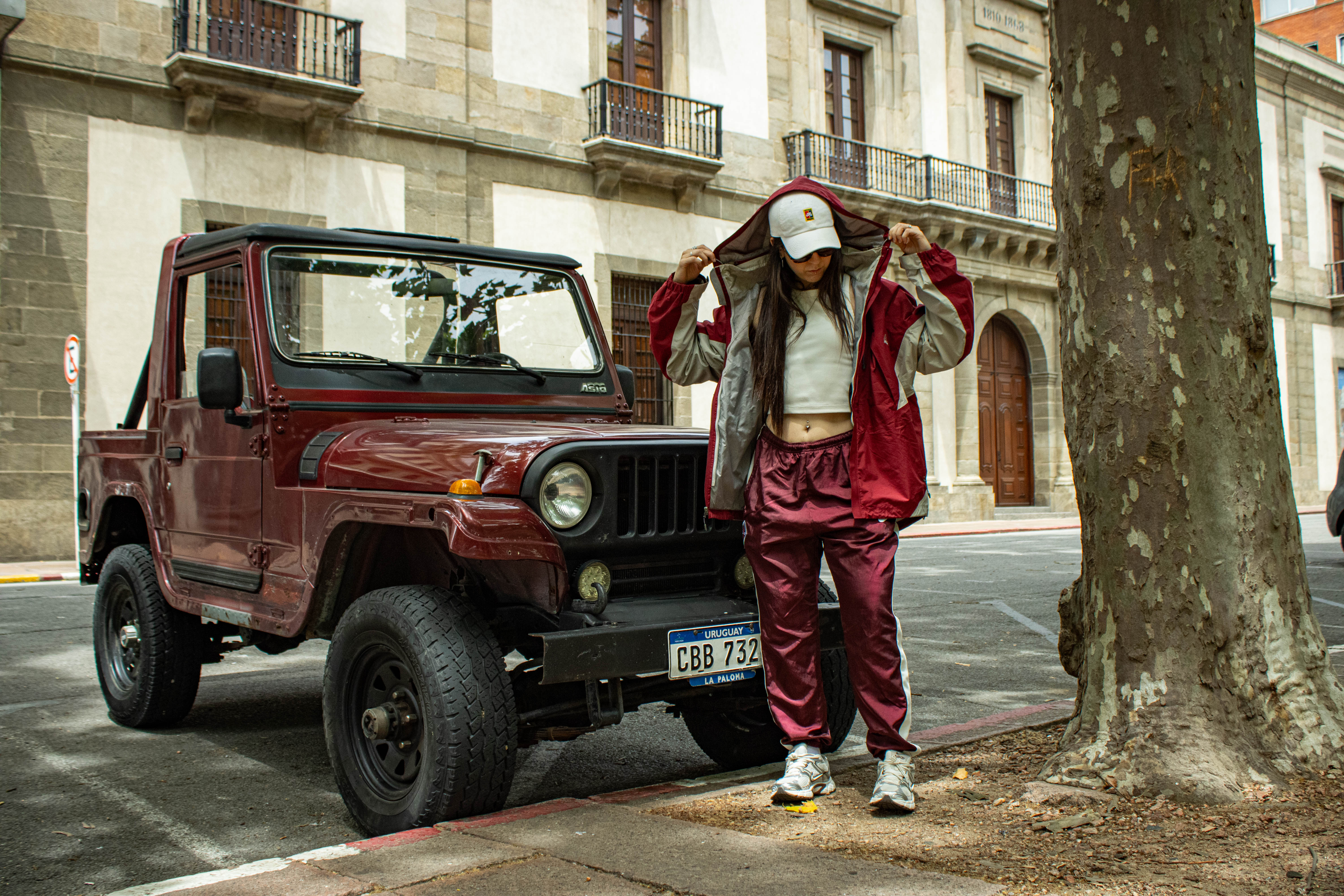 Chica con campera burdeos junto a Jeep del mismo color — klok curated secondhand