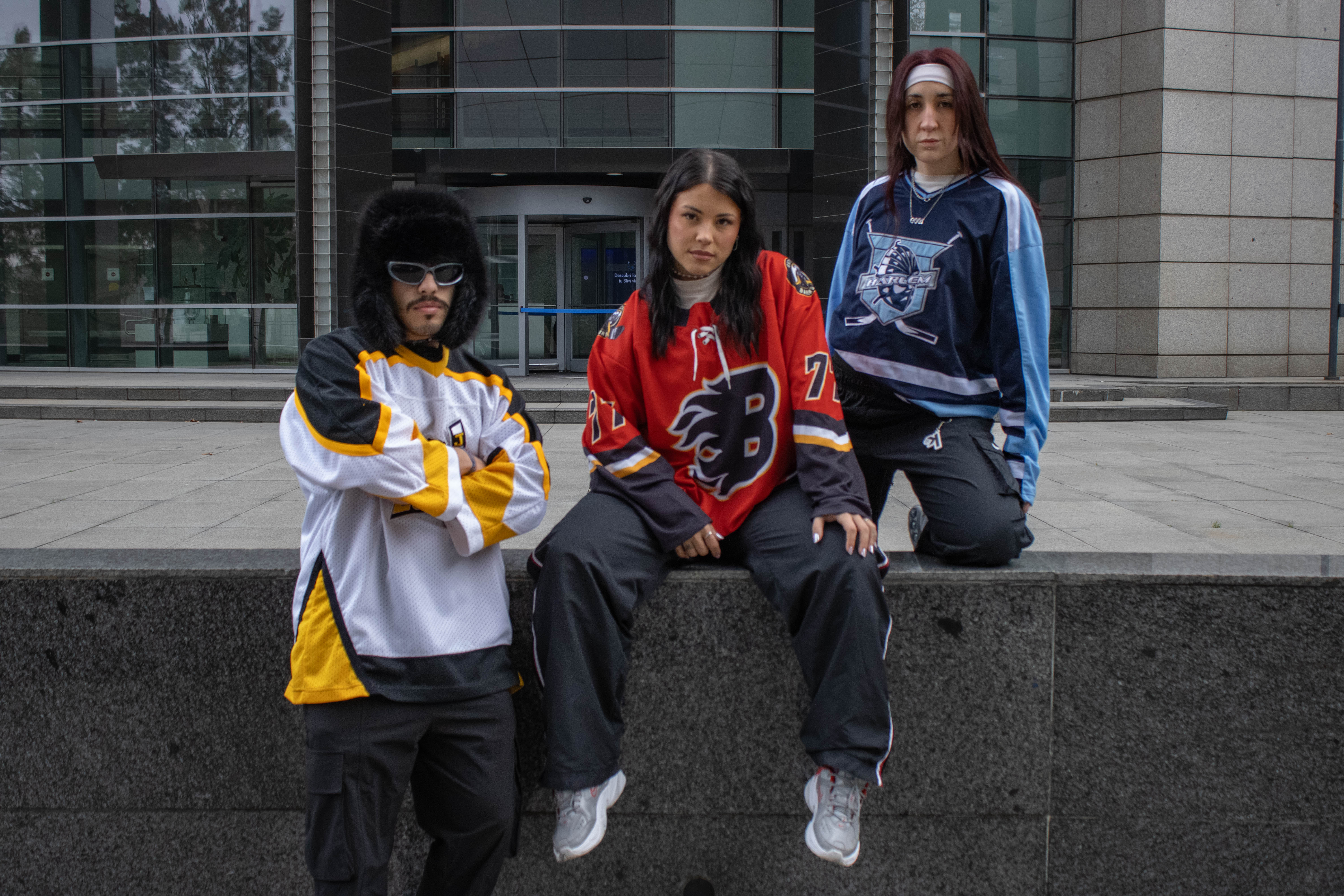 Tres amigos con jerseys de hockey vintage frente a un edificio de vidrio — klok curated secondhand