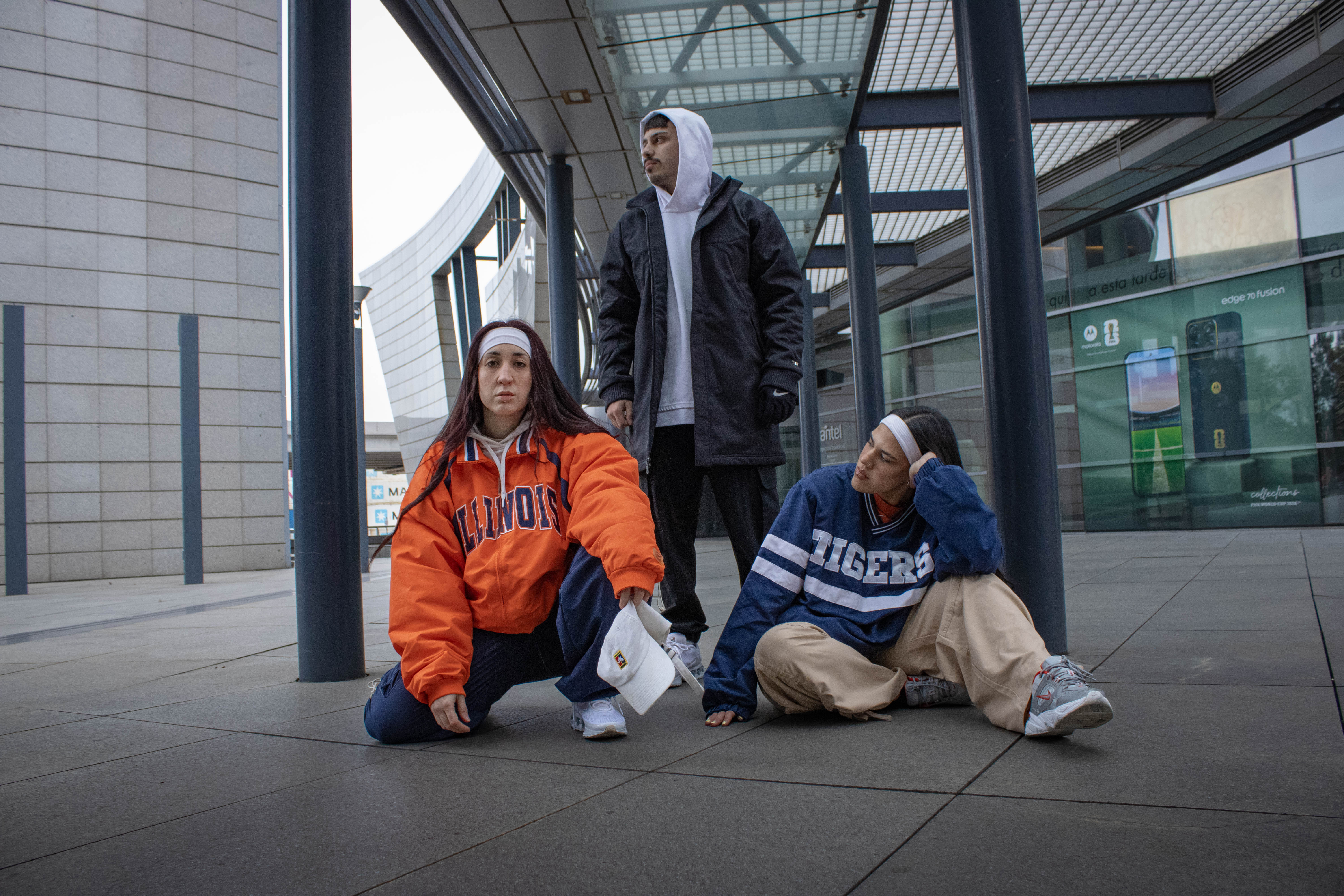 Dos chicas con buzo universitario Illinois y jersey Tigers junto a un chico con campera negra — klok curated secondhand
